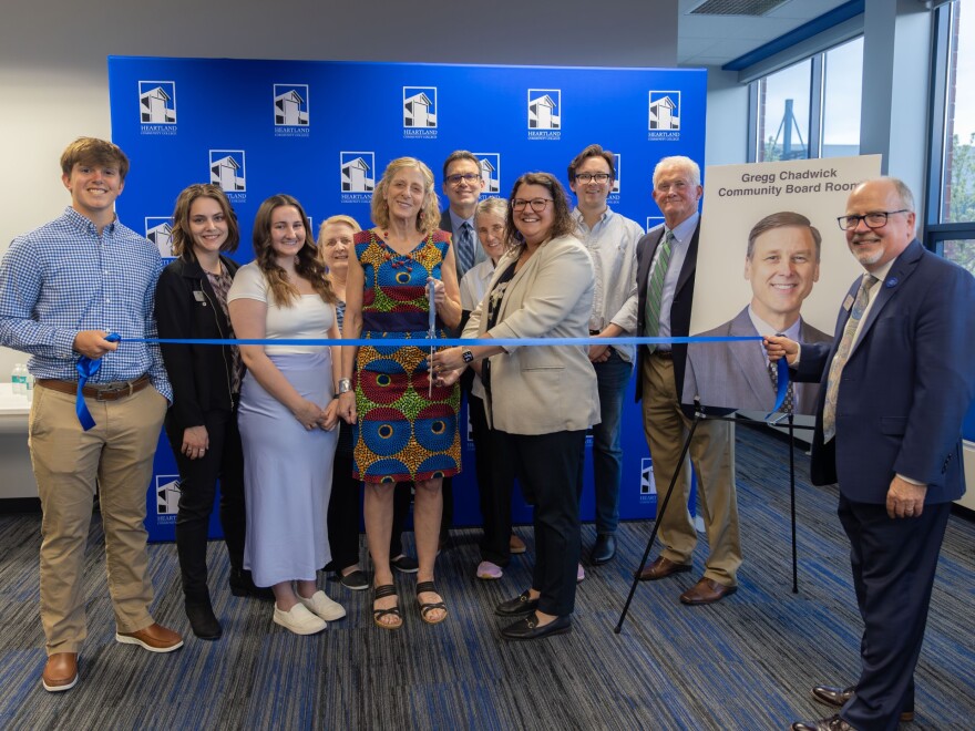 A group of people stands behind a ribbon getting ready to cut it