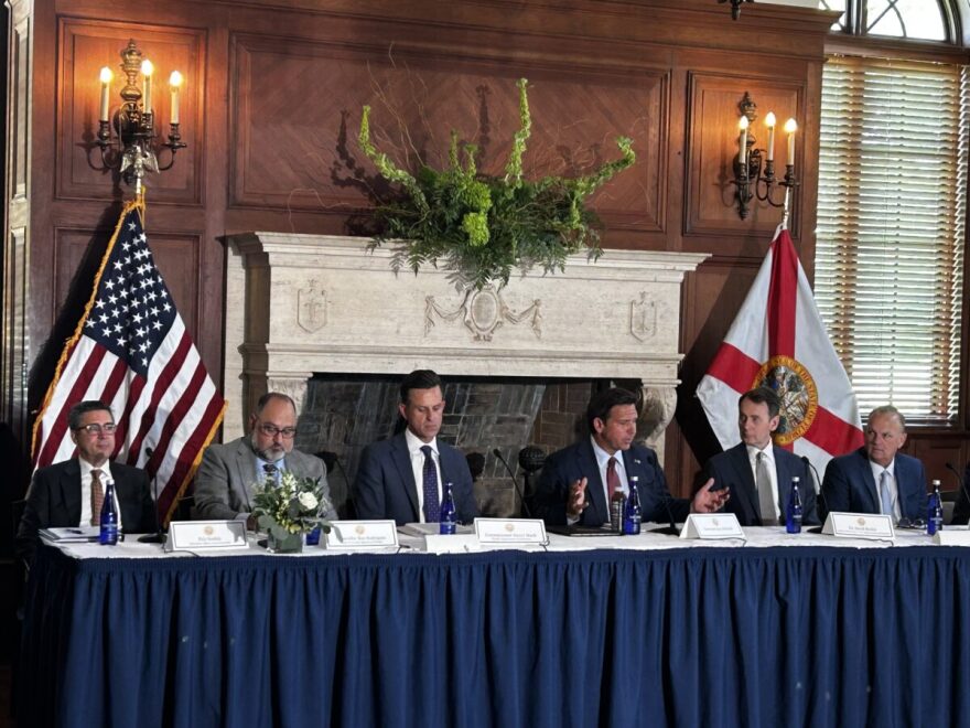 A panel of politicians sitting at a blue table with flags behind them 