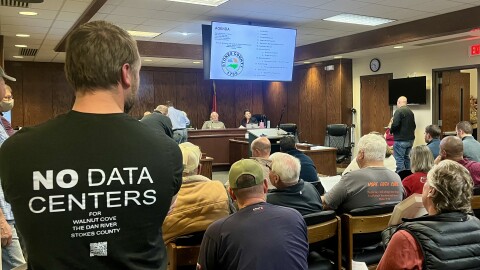 A man wearing a "no data centers" shirt stands among the crowd at a Stokes County Board of Commissioners meeting