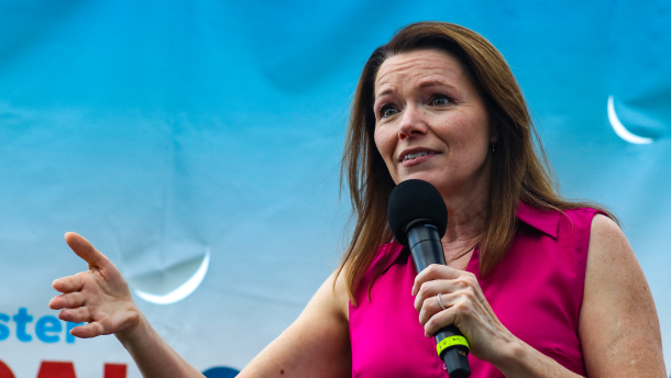 A woman in a bright pink shirt holds a microphone.
