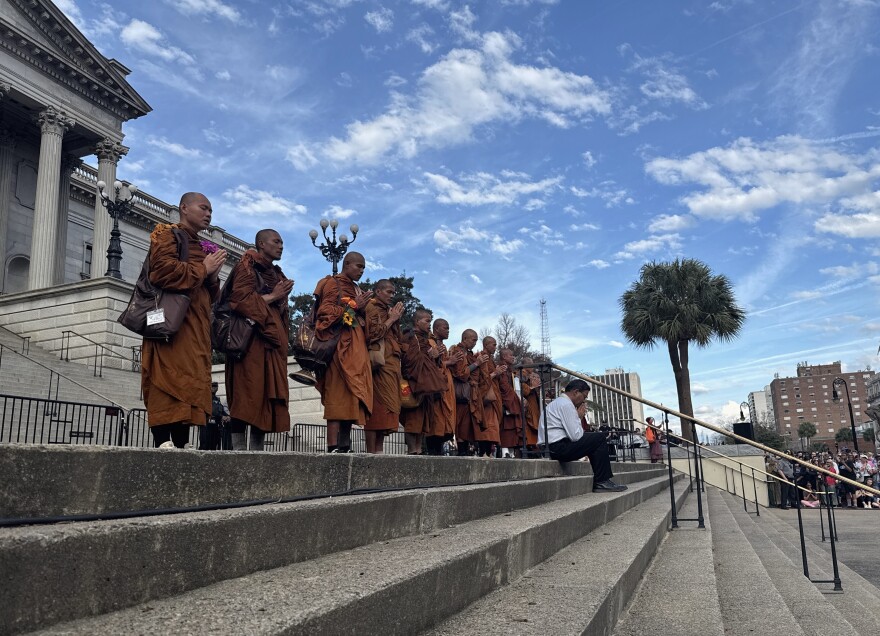 Seventeen Buddhist monks stand in line on the South Carolina Statehouse's steps.