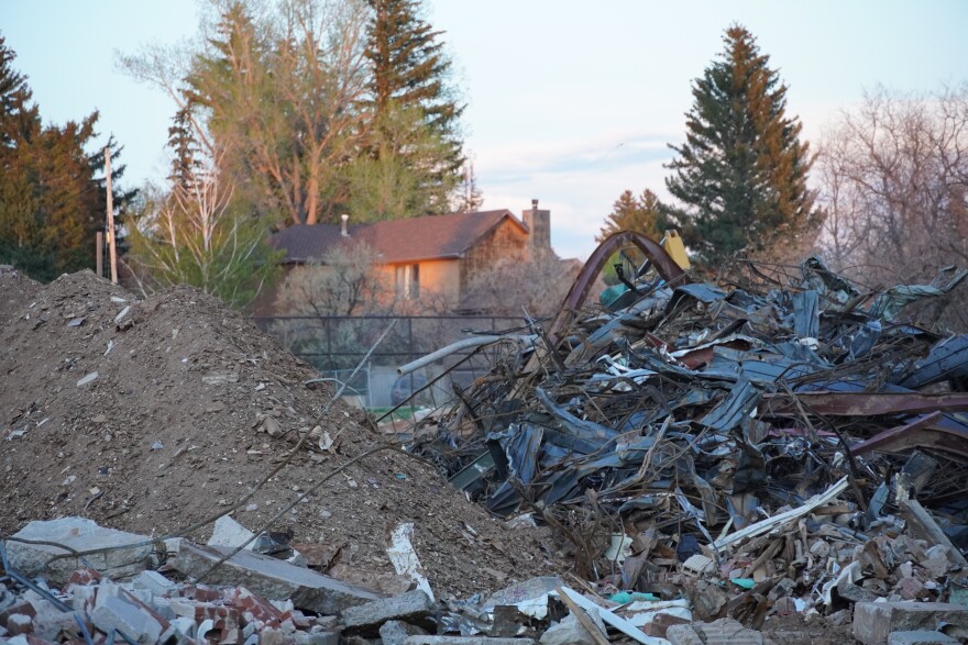 Mounds of demolition debris are visible in front of a house in the background.
