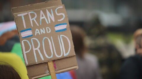 Closeup photo of a cardboard sign in a crowd that reads "Trans and Proud."