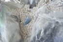 A blue battery is encased in a clear plastic bag and surrounded by white fire-suppressing beads. 