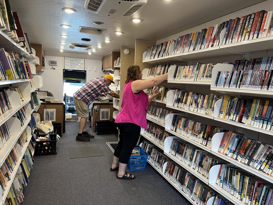 Two librarians shelve books inside a bookmobile.