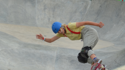 A skateboarder carves in a concrete bowl.