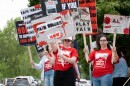 Men and women wearing red shirts hold signs on a street corner.