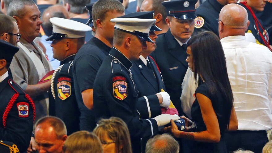 Juliann Ashcraft, wife of late firefighter Andrew Ashcraft, receives a U.S. flag during a memorial service in July. Ashcraft says the city has refused to pay full benefits for her husband's death, calling him a seasonal employee.