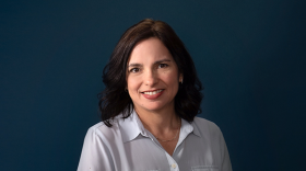 A person smiling into a camera against a dark backdrop. 