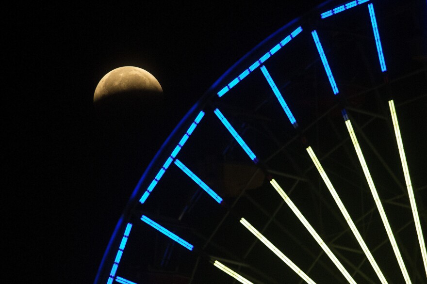 The lunar eclipse progresses behind a ferris wheel over Santa Monica Beach in Santa Monica, Calif., on Wednesday. The first total lunar eclipse in more than two years is coinciding with a supermoon.