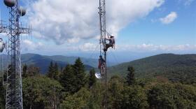 two workmen atop a radio tower in the lush woods of Western North Carolina
