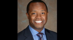 A portrait of Catlin, in dark suit jacket, blue shirt and purple-blue tie with silver highlights.