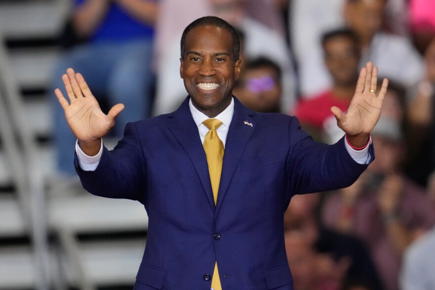 A smiling man in a suit extends his arms out in front of him during a rally.