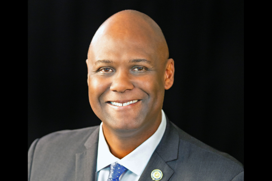 Ray Curry, a Black man wearing a suit smiling at the camera. We see him from the shoulders up