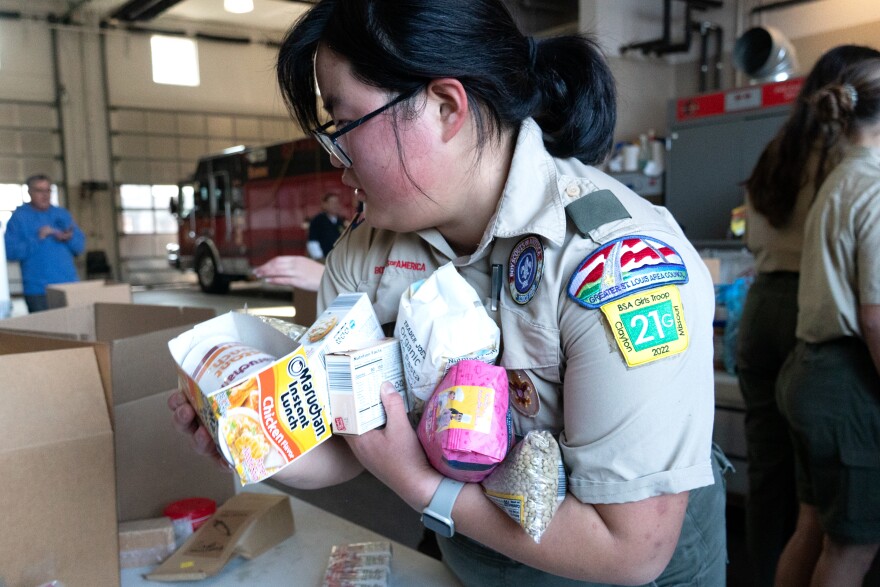 Scout Yuhan Liu, 14, of Troop 21G fills her arms with non-perishable food items and carries the items to a sorting bin located at a local fire station in Clayton, Mo.