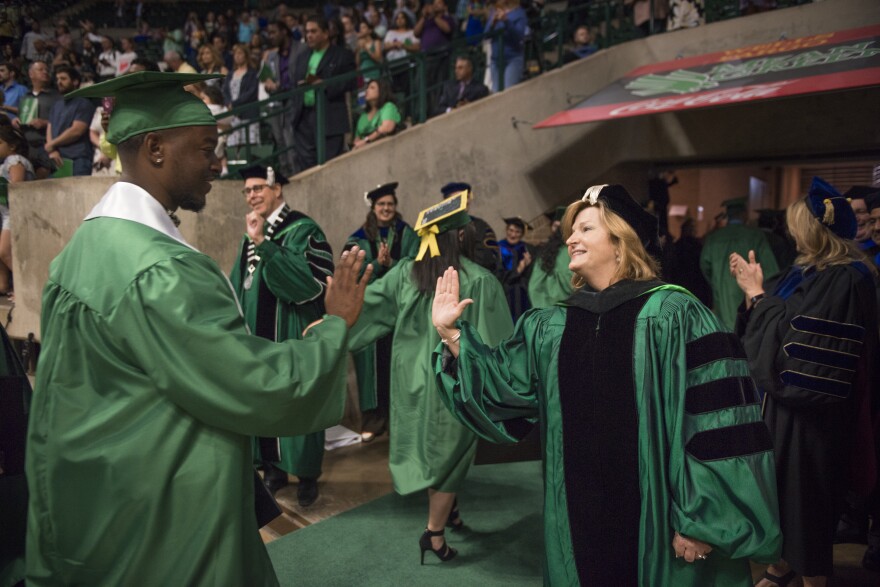 University of North Texas System Chancellor Lesa Roe high fives a student in a cap and gown. 