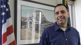 Tacoma Mayor Anders Ibsen stands in front of a painting and alongside the U.S. and Washington flags.