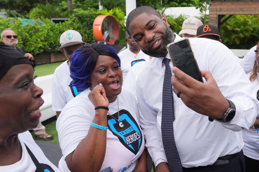Black man in white dressshirt and tie  leans over to take a smartphone selfie with a shorter black woman in a white tshirt
