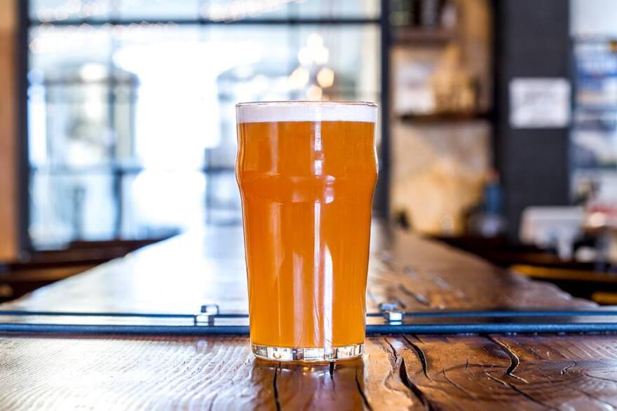 A pint of beer on a wooden bar table.