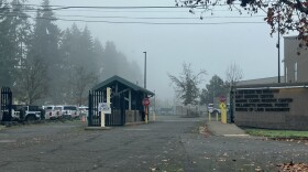 An entrance to a government facility. There is a guard house and a stop sign. 