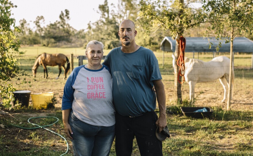 Susan Koppelman, 52, and Keith Koppelman, 49, stand for a portrait at a rural property outside Marianna, Fla., where they have been staying since being evicted from their trailer home after last year's hurricane. The landowners allow the couple to live in the storm-damaged house rent-free in exchange for help with the horses.