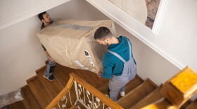 Professional movers moving up on staircase and carrying large box with furniture on first floor of house