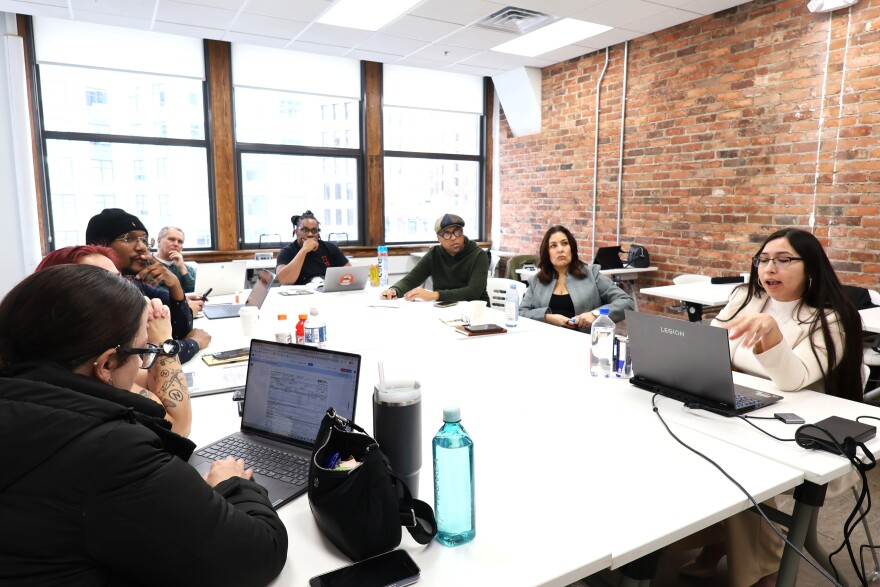 Employees of Nation Outside gather around laptops and a large screen TV to discuss what they’ll teach during their digital literacy courses.