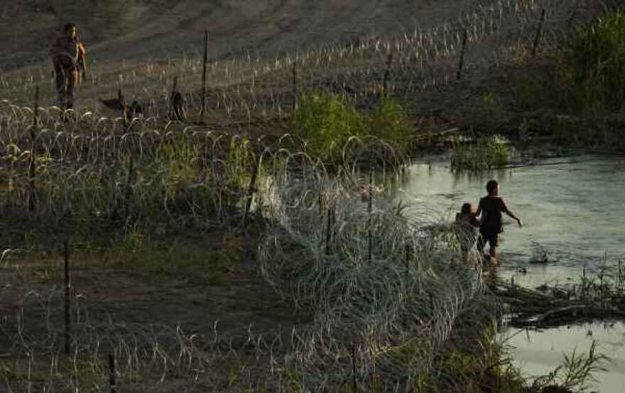 Un policía de Texas habla con migrantes mientras caminan a lo largo de alambre de púas e intentan cruzar el Río Grande en la frontera entre Texas y los Estados Unidos en Eagle Pass, Texas, el jueves 6 de julio de 2023.