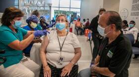 Ron Book (far right) Chairman of the Homeless Trust looks on as a medical staff vaccinates Janet Bristol, who got her second round of covid vaccines at Jackson Memorial as part of a partnership program between the Homeless Trust and the Jackson Memorial Hospital to vaccinate senior citizens who are homeless and/or housed in permanent housing. on Friday, February 19, 2021.