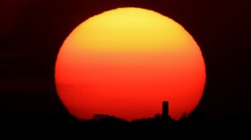 A distant smokestack stands against the setting sun in Kansas City, Mo., Friday, June 26, 2020. Sunsets and sunrises are more vibrant than usual lately due to dust in the atmosphere from a Saharan dust cloud. (AP Photo/Charlie Riedel)