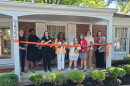 people stand on house porch and cut an orange ribbon with comically large scissors