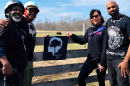 Four Black outdoor enthusiasts stand in a field beside a wooden fence.