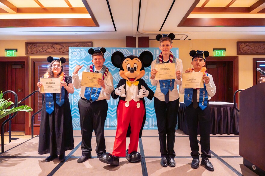 Four people wearing Mickey Mouse ears and graduation gear with Mickey Mouse standing in the middle 