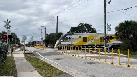 A Brightline train passes behind a crossing gate on WH Jackson Street in Melbourne, where company workers have added traffic delineation posts to deter drivers from trying to drive around the gate when it's down.