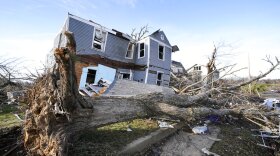 FILE - An overturned tree sits in front of a tornado-damaged home in Mayfield, Ky., on Dec. 11, 2021. Gov. Andy Beshear traveled to an event in hard-hit Mayfield on Friday, June 10, 2022, to celebrate the first fully constructed new homes since the town took a direct hit from a tornado last December. (AP Photo/Mark Humphrey, File)