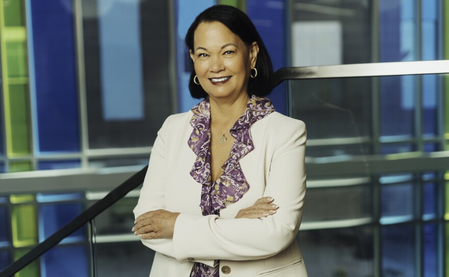 Ebert is standing with her arms crossed, smiling and wearing a purple shirt and a white jacket. 
