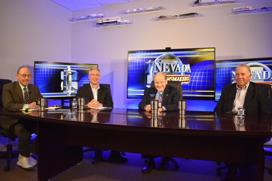 Four men in suits sit at a table, smiling for a photo. Behind them are three television screens with a graphic that reads, “Nevada Newsmakers.”