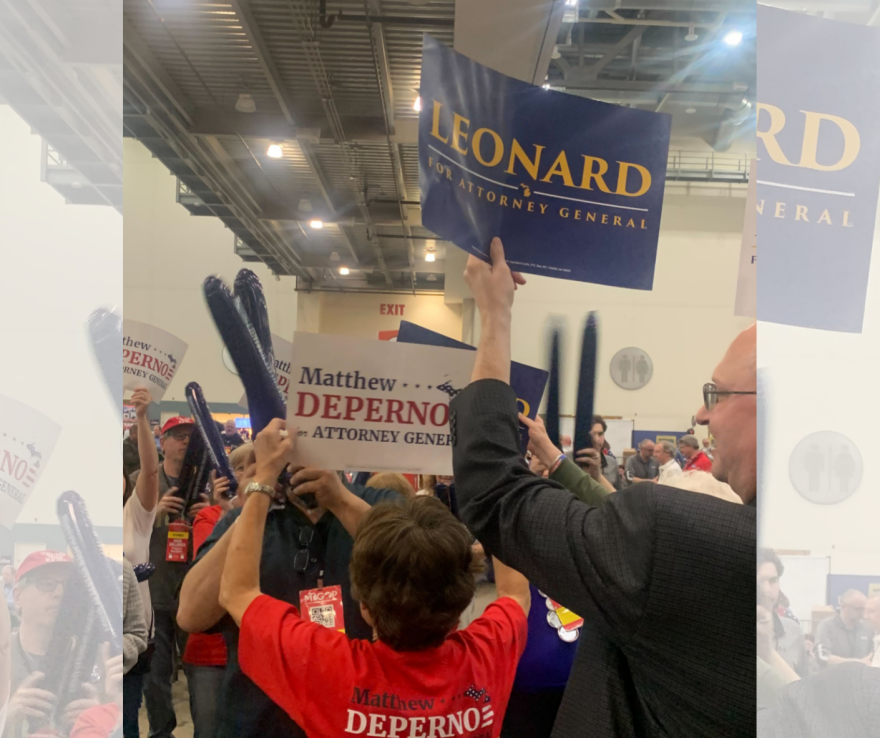 A group of people at the April 2022 Michigan Republican Party nominating convention. Some are holding signs supporting Matthew DePerno for attorney general and others are holding up signs supporting Tom Leonard for attorney general. 