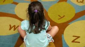 A child sits on a multi colored rug 