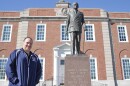 A man wearing a blue windbreaker stands in front of a courthouse. There is a statue of Harry Truman next to him.