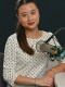A person sits inside a radio studio. They are sitting behind a microphone and looking at the camera, smiling.