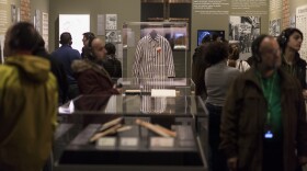 people look at museum exhibit. a prison uniform is at center