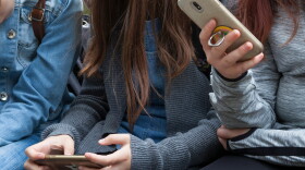 Two young teenage girls sitting holding smartphones in their hands.
