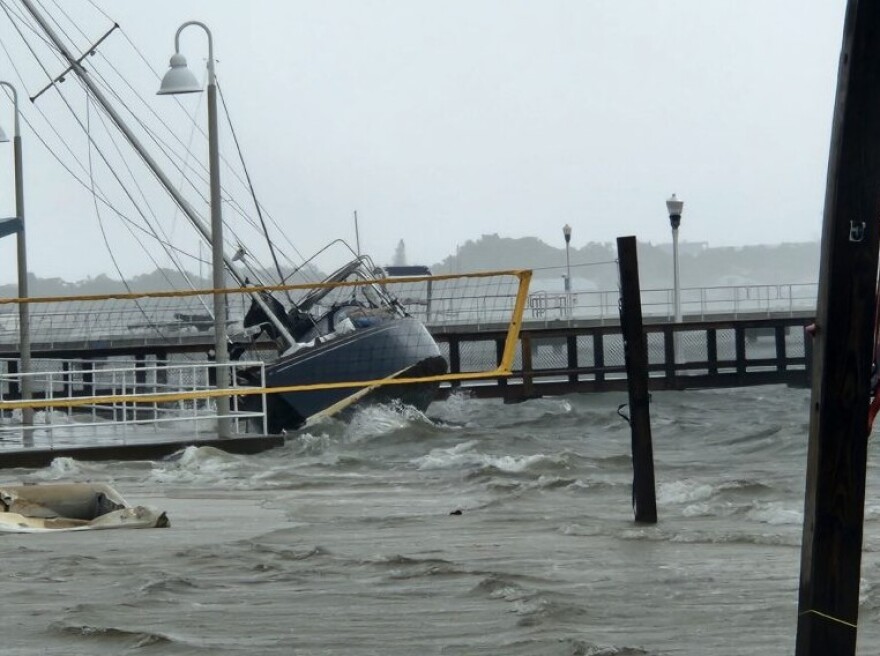 A sailboat was wedged underneath the Municipal Pier, behind the Gulfport Casino, after Hurricane Helene. You can see the boat tilted behind a flooded volleyball court with water crashing around.