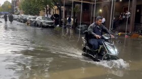 In this photo taken from video, a man drives a scooter through flood waters, Friday, Sept. 29, 2023, in the Brooklyn borough of New York. A potent rush-hour rainstorm swamped the New York metropolitan area. The deluge Friday shut down swaths of the subway system, flooded some streets and highways, and cut off access to at least one terminal at LaGuardia Airport. 