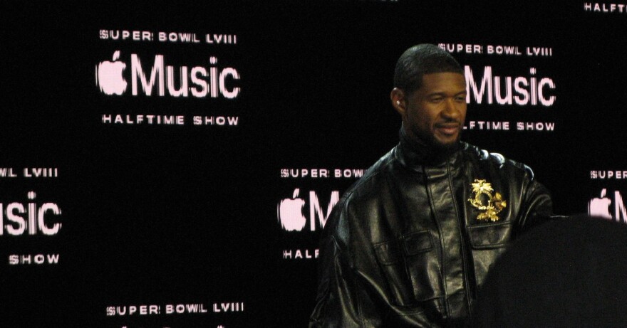 Usher poses for the crowd in front of a black background. 