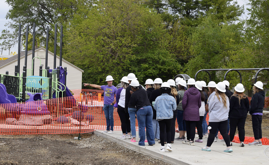 Man points toward playground in front of more than a dozen teachers in hard hats.
