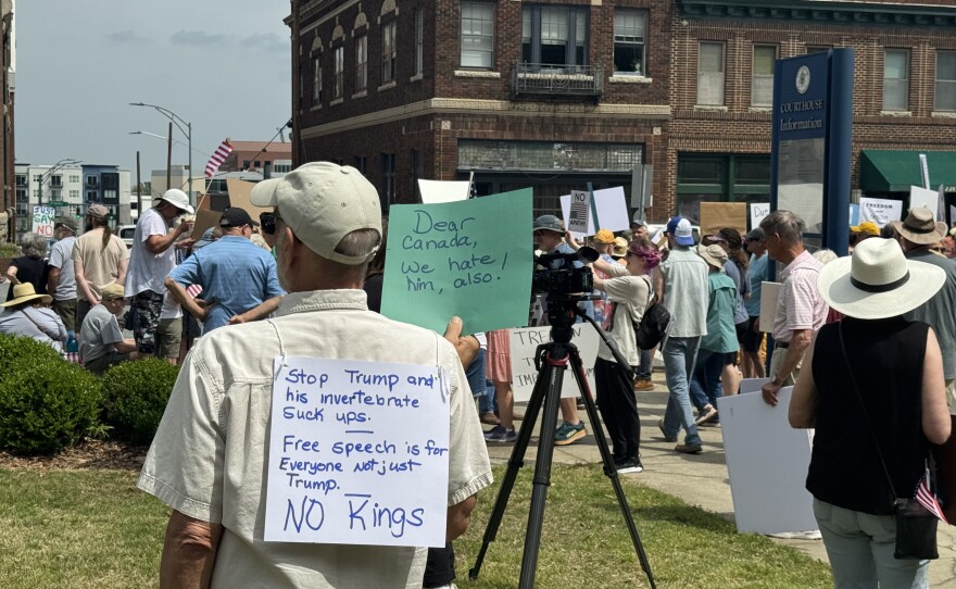 A photo of a man holding a sign at a rally against Trump 