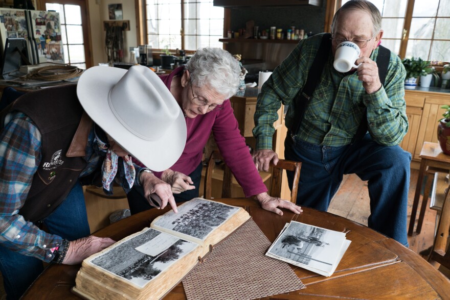 Three people look at an old photograph album.