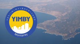 A logo with a blue ring and white text, and a yellow center with white buildings in silhouette and blue letters. Behind it is an aerial view of water with a landmass.